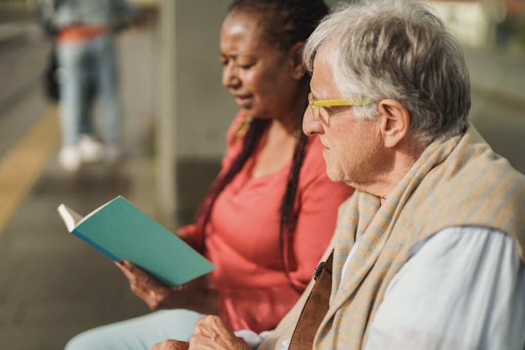 Two adults reading together on a bench, supporting adult literacy through shared learning.