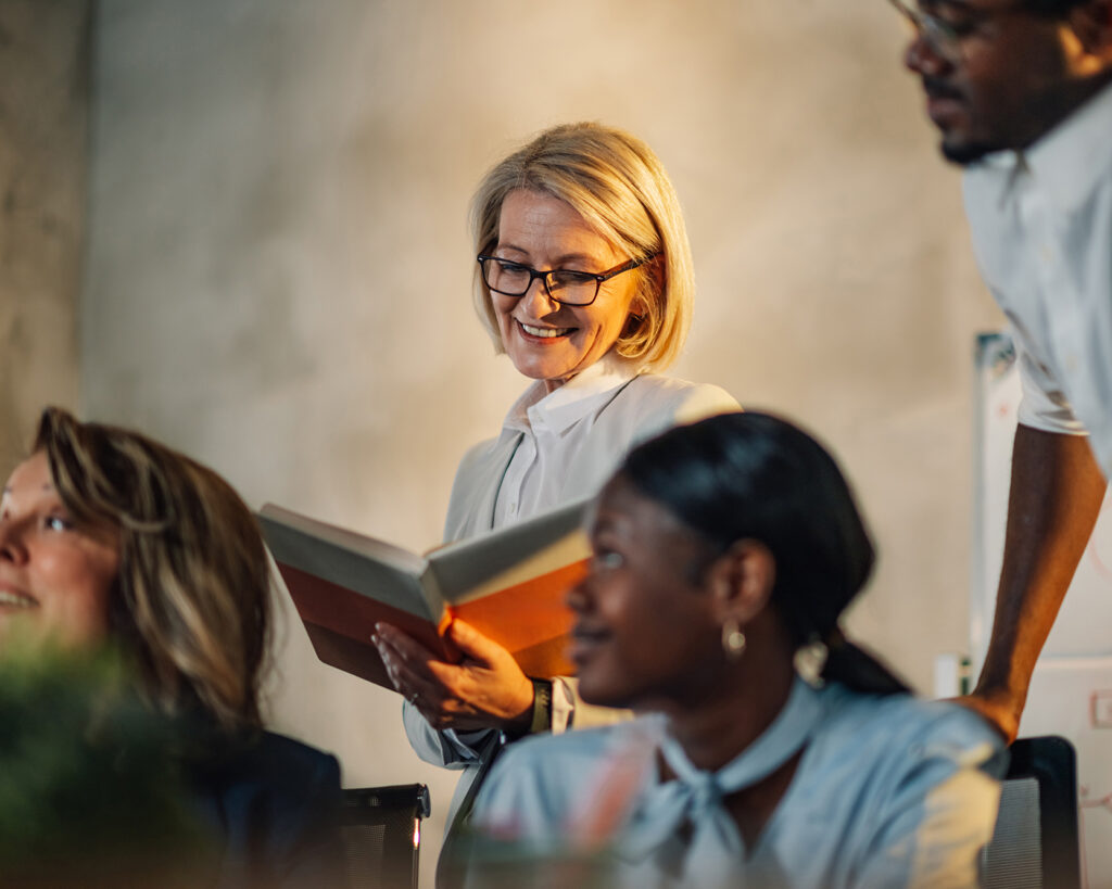 Smiling instructor reading from a book to diverse adult students during adult learning classes.