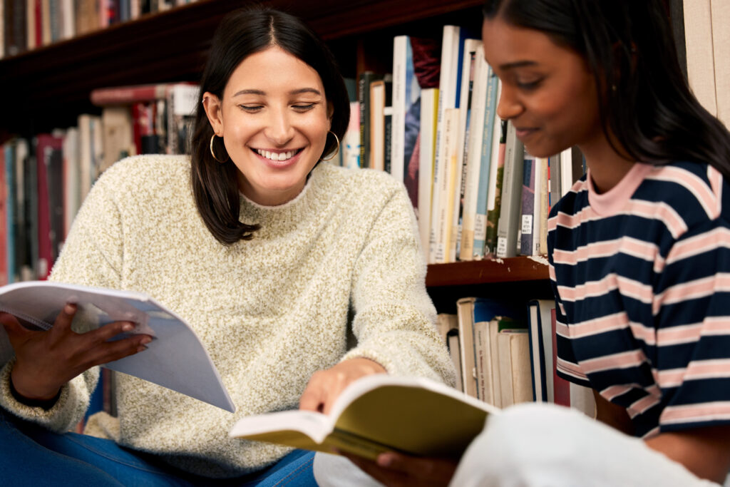 Two young adult women smiling and reading together in an adult education program supported by a nonprofit fundraiser.